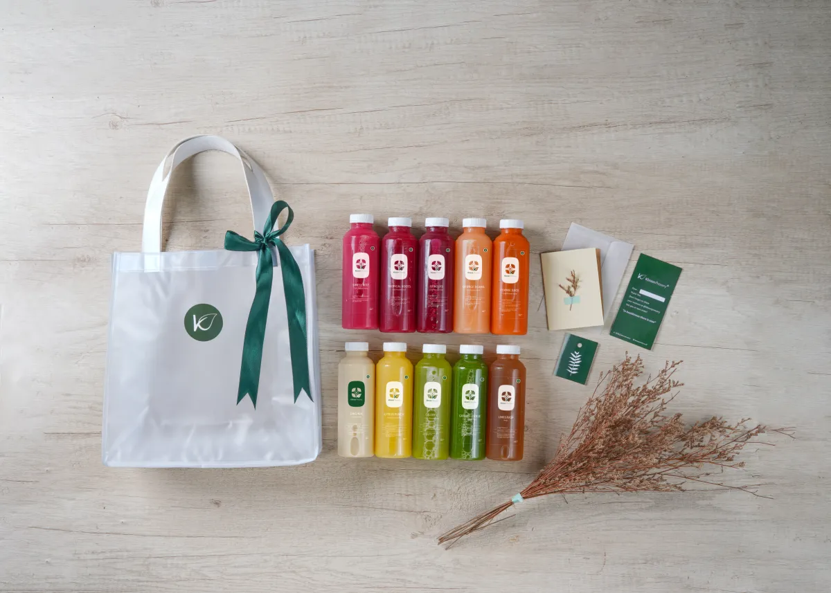Hampers besar Kboon: tas kain berpita hijau, dua baris botol jus, dan kartu ucapan