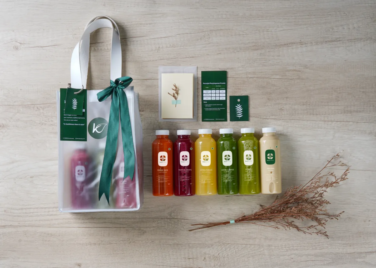 Hampers sedang Kboon: tas kain berpita hijau, deretan botol jus, dan kartu ucapan