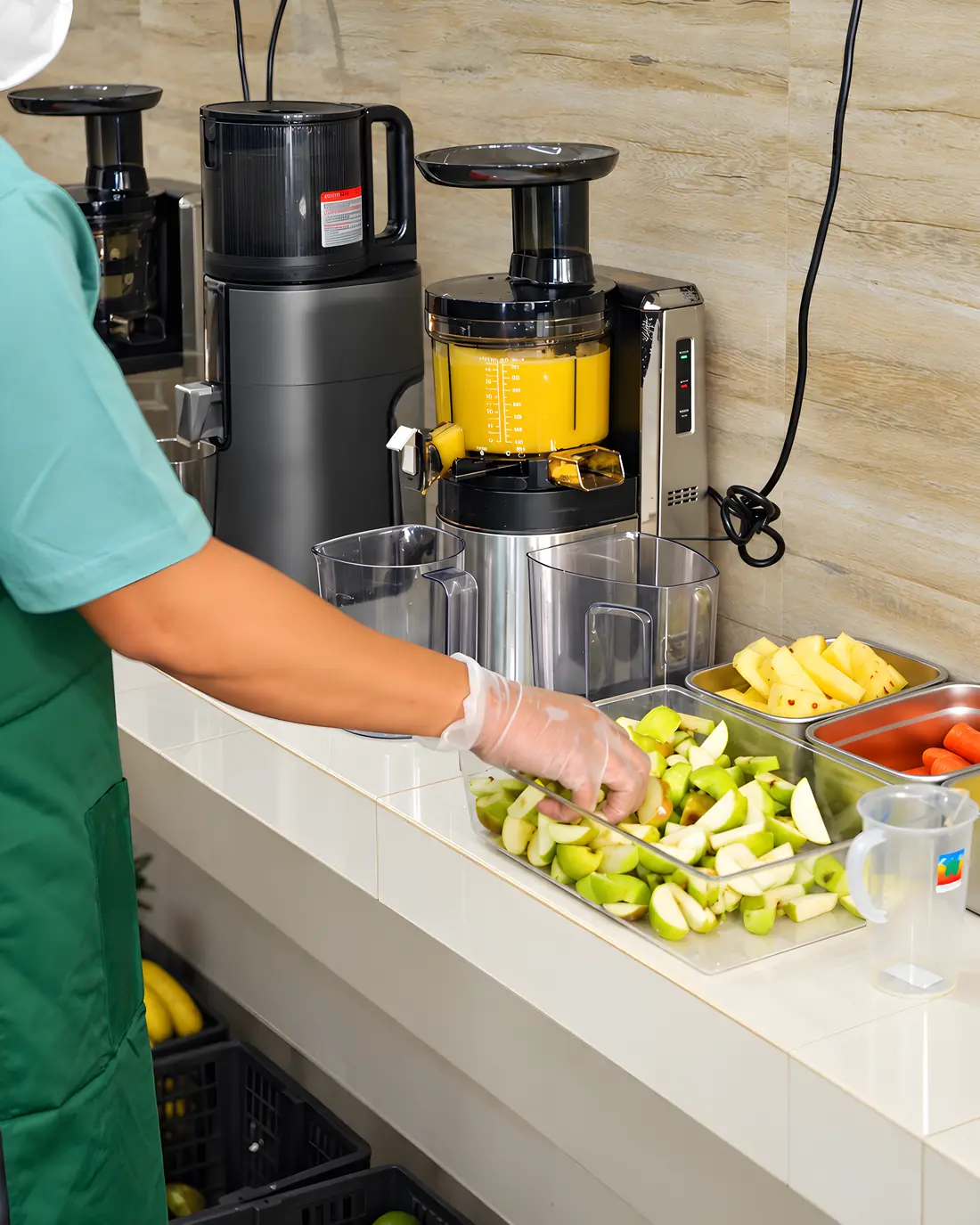Mesin cold press memeras jus kuning, potongan apel hijau siap di sampingnya